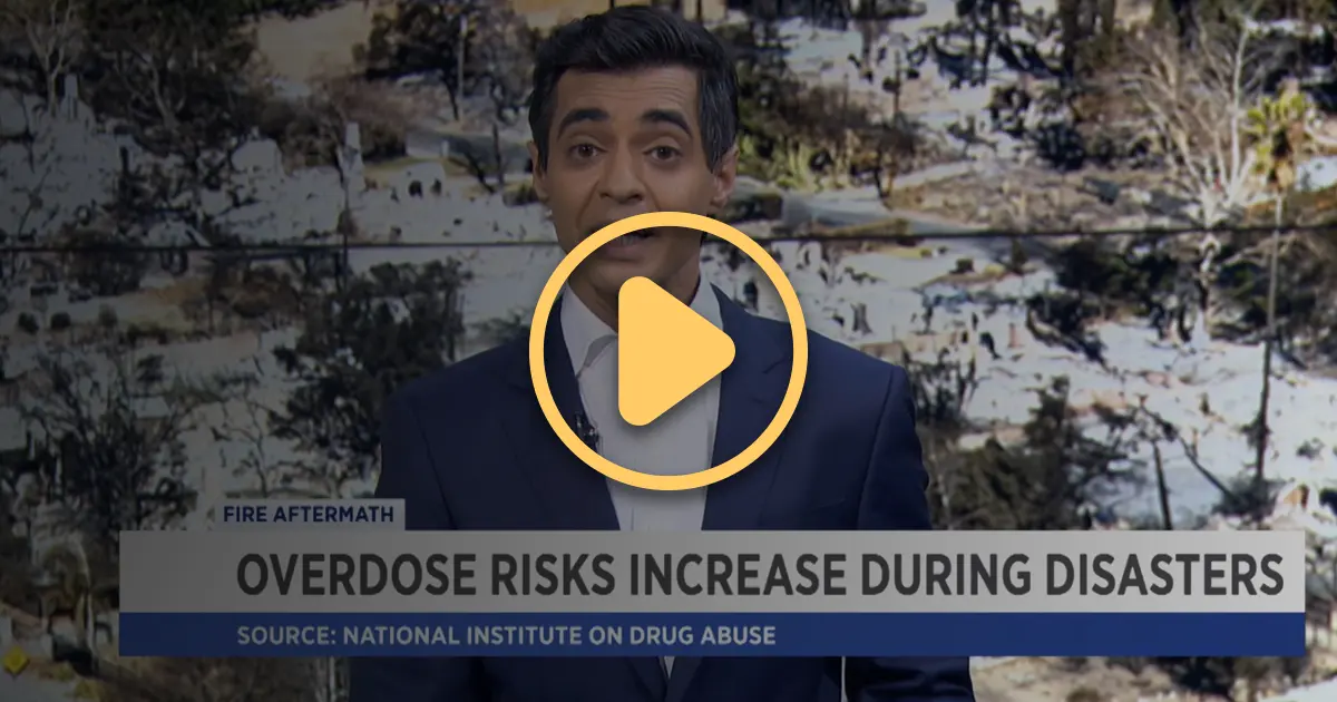 A newscaster in a television studio with a backdrop showing photos of the aftermath of the Los Angeles Fires in 2025.
